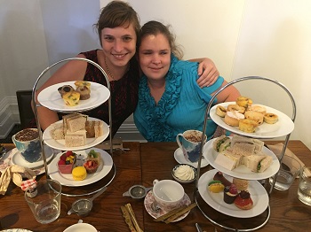 Image shows Rachael left and Hailey right arms around each other and high tea food on three tiered plates in front of them