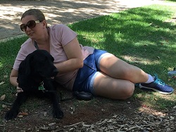 Tarhnee lying down laterally and partially upright on grass with dog guide Jules being patted