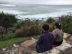 Hailey and Gabbi sitting on a stone seat looking above and out towards the ocea