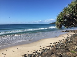 Image taken at Byron Bay looking at sand, rocks in foreground, and beautiful ocean expanse ahead