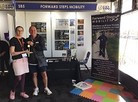 a photo of Kim and Tony standing side by side to left of Forward Steps Mobility booth with Tony showing his medal