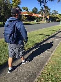 a picture Side and rear profile of a man walking along a residential footpath using his long cane