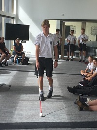 a school boy with his cane walking with his eyes closed