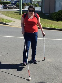 Frances crossing a road with long cane and support cane