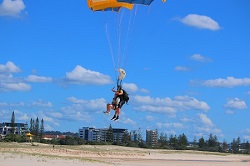 A terrific side on photo of George tandem skydiving meters above the sand preparing to land