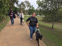 Group Emerald Lakes, Hailey walking with dog guide in nature setting with others following behind with dogs and canes