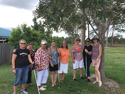 Eight ladies standing side by side in a green park, with three long canes visible