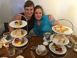 Hightea Hailey and Rachael Sitting side by side with three tiered high tea plate setting in front filled with food