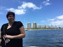 Jordy on front of a boat smiling, with broadwater and high rise apartments behind her
