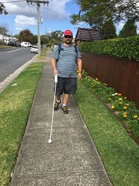 Justin walking along a residential path with a long cane